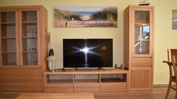 Ett vardagsrum med en TV-möbel i trä, en platt-TV och en tavla med strandmotiv ovanför.