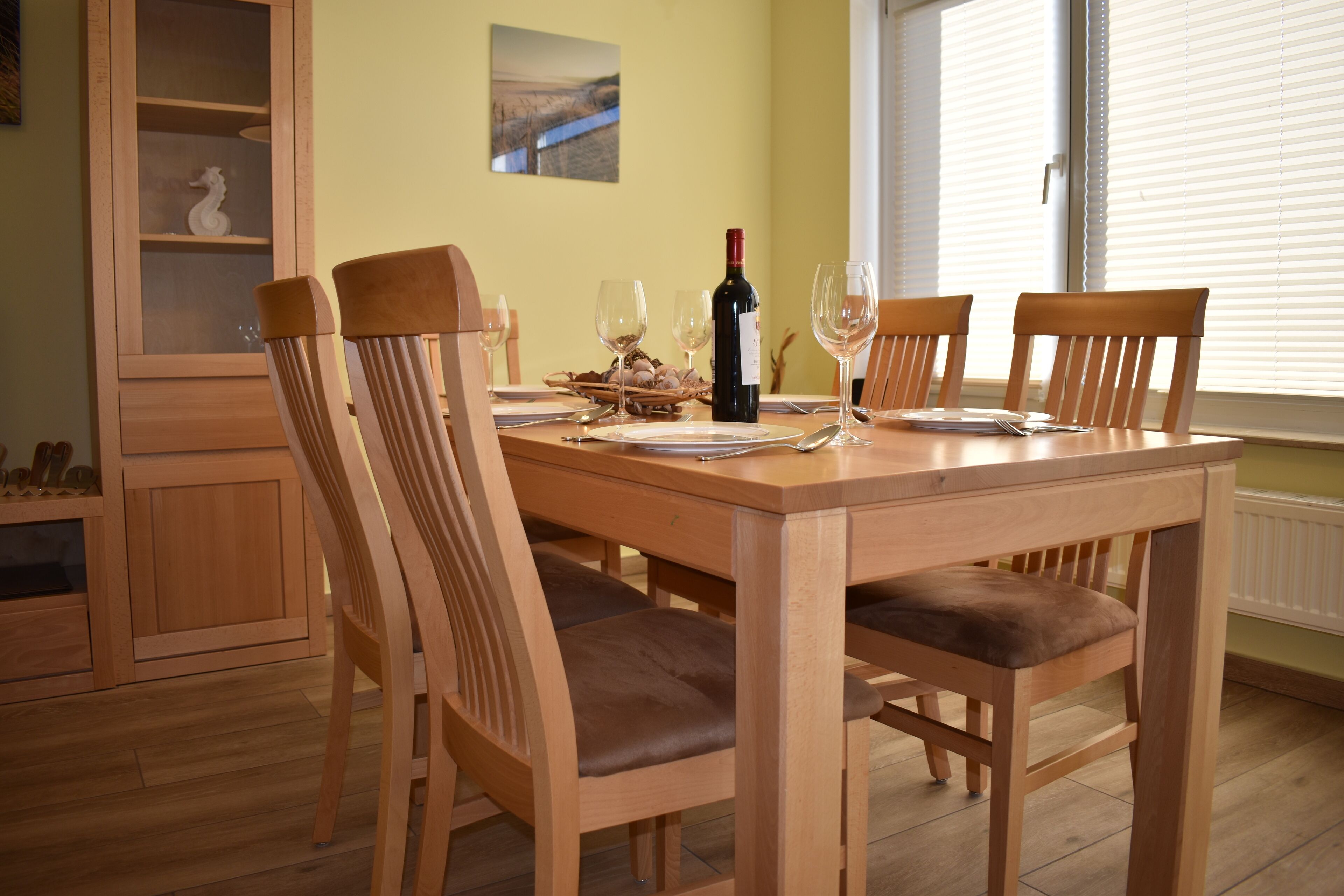 Een eettafel met houten stoelen, een fles wijn en wijnglazen.