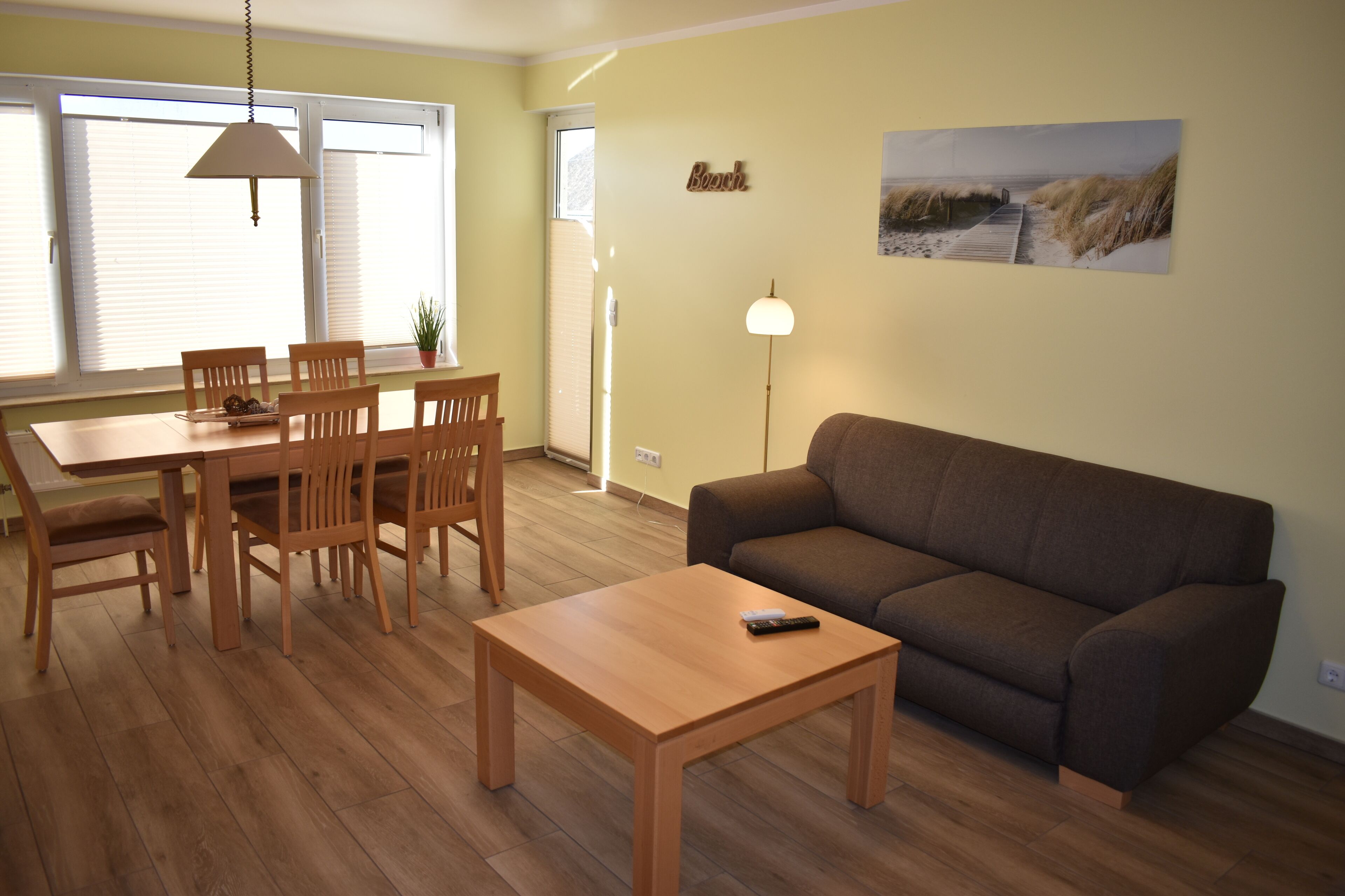 Un salón con una mesa de comedor de madera, sillas, un sofá marrón y una lámpara.