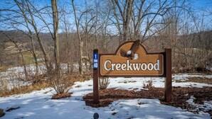 A wooden sign with the name "Creekwood" and a bird illustration, surrounded by bare trees and snow.