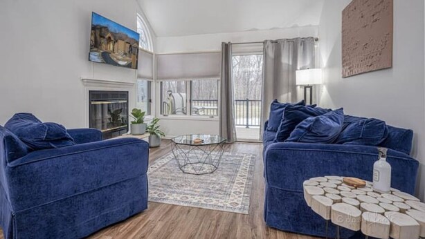 A living room with two blue sofas, a glass coffee table, a patterned rug, and a wooden side table.