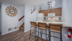 A modern kitchen with wooden cabinets, a white countertop, and a large clock on the wall.
