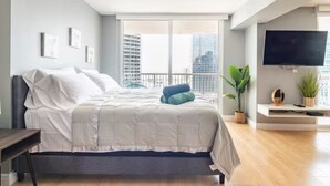 Ein modernes Schlafzimmer mit einem großen Bett, einem an der Wand befestigten Fernseher und einem Balkon mit Blick auf die Stadt.