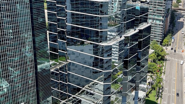 Ein Hochhaus mit moderner Glasfassade, mehreren Balkonen und einem Parkplatz mit Autos.