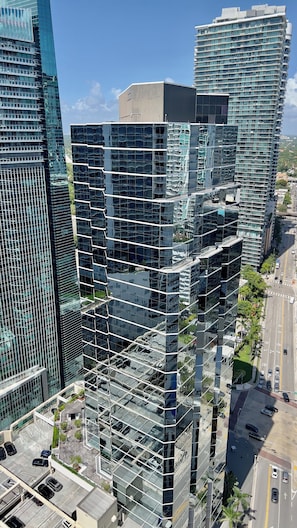 A high-rise building with a modern glass facade, multiple balconies, and a parking area with cars. - Brickell Center w/City & Bay View + FREE Parking! (Miami)