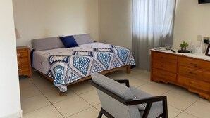 Une chambre à coucher avec un lit, une chaise, une commode, un téléviseur et une fenêtre avec des rideaux.