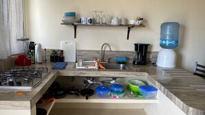 Une cuisine équipée d’une cuisinière à gaz, d’un évier et de divers ustensiles. On y trouve également un distributeur d’eau et une machine à café sur le plan de travail.