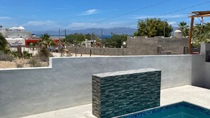 Une piscine agrémentée d’un mur en pierre, entourée d’une terrasse en béton et d’un petit muret, offrant une vue dégagée sur la mer et les montagnes lointaines en arrière-plan.