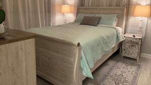Un dormitorio con una cama de madera, dos mesitas de noche con lámparas, una alfombra y cortinas de gasa.