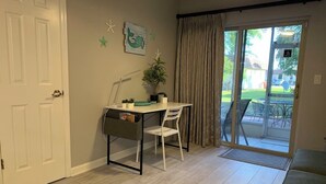 Una habitación con escritorio, silla y vista a un jardín trasero a través de una puerta corrediza de vidrio.
