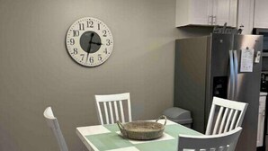 Un comedor con una mesa, sillas, un reloj de pared y una cocina al fondo.