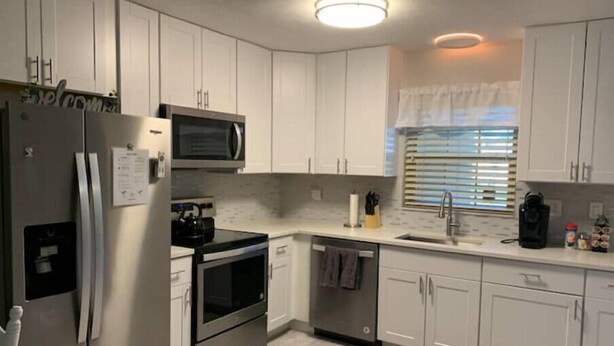 Una cocina moderna con armarios blancos, electrodomésticos de acero inoxidable y una ventana con persianas.