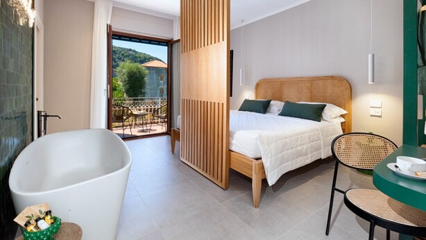 Une chambre d’hôtel moderne dotée d’une grande baignoire, d’une cloison en bois, d’un lit avec une literie blanche et d’une vue sur l’extérieur.