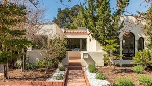 Una casa moderna con un sendero que lleva a la entrada, rodeada de un jardín con plantas y árboles diversos.