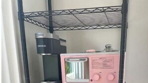 Una cocina con cafetera, tostadora y microondas sobre una estantería de metal negro.