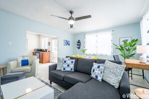 A living room with a grey sofa, a dining table, and a ceiling fan.