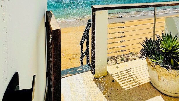 Blick auf einen Strand mit einer Brause, einem hölzernen Geländer und einem Topfpflanzen.