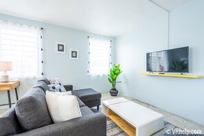 A modern living room with a grey sofa, a white coffee table, and a flat-screen TV on a yellow shelf.