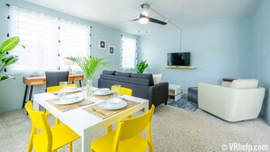 Ein modernes Wohnzimmer mit Essbereich, einem grauen Sofa, einem weißen Sessel und einem Deckenventilator.