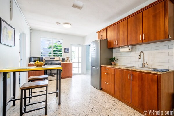 A kitchen with wooden cabinets, a stainless steel refrigerator, a sink, and a dining area with a table and chairs. - Roadside Apartment of Beachfront Property! AC & WiFi (Rincon)