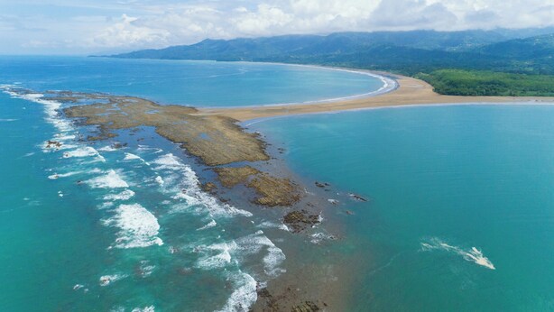 An aerial view of a coastal area with clear blue waters, a sandy beach, and green hills in the background. - Cozy house, pool, WIFI, mins to beach, Uvita (Ballena)