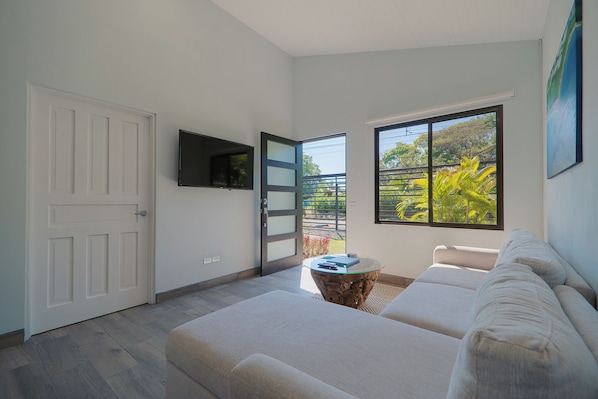 A modern living room with a sofa, a coffee table, a TV, and a large window with a view of greenery.