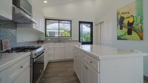 A modern kitchen with white cabinets, a large island, a stove, and a window with a view of greenery. - Cozy house, pool, WIFI, mins to beach, Uvita (Ballena)