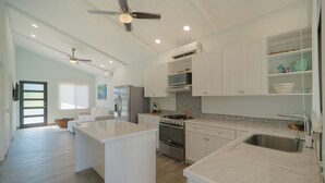A modern kitchen with white cabinetry, a central island, and a stainless steel sink. - Cozy house, pool, WIFI, mins to beach, Uvita (Ballena)
