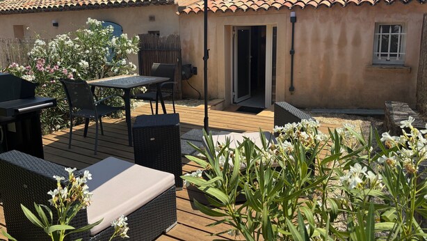 Un patio con mobiliario exterior, una sombrilla blanca y una puerta que da a una zona cubierta.