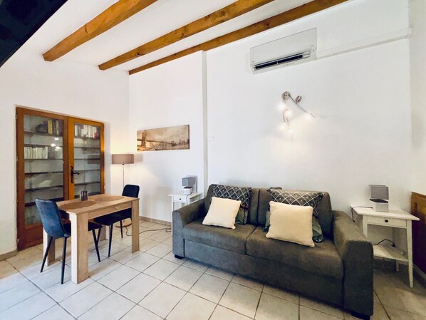Una sala de estar acogedora con un sofá, una mesa de comedor con sillas, una estantería y un cuadro en la pared.