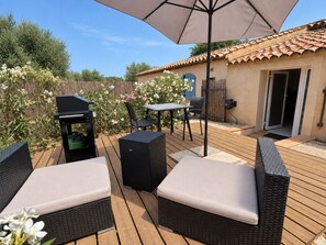 Een terras buiten met rieten meubilair, een tafel en een barbecue.