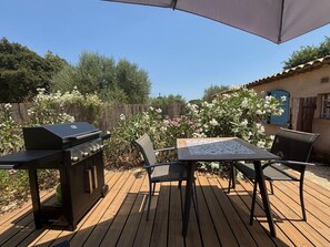 Een terras buiten, met een barbecue, een tafel en stoelen.