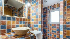 Un baño con un lavamanos grande y redondo, un espejo y paredes de azulejos coloridos.