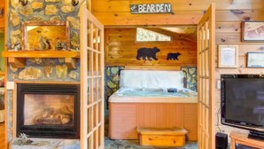 A cozy cabin interior with a stone fireplace, a hot tub, and a television. - Katahdin Cabin Rustic Romance + Indoor Hot Tub Near Town (Blue Ridge)