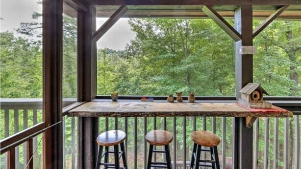 A wooden deck with a railing, a table with bird feeders, and three stools. - Katahdin Cabin Rustic Romance + Indoor Hot Tub Near Town (Blue Ridge)
