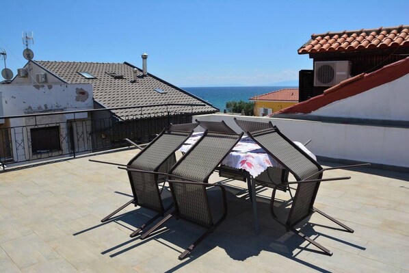 Une terrasse sur le toit, avec une table et des chaises, une vue sur la mer et un bâtiment doté d’un toit en tuiles.