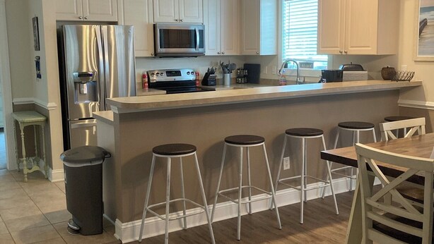 Una cocina moderna con armarios blancos, electrodomésticos de acero inoxidable y una isla central con taburetes de bar.