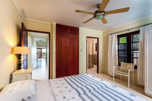 A bedroom with a bed, a ceiling fan, a nightstand, a chair, and a view of a bathroom.