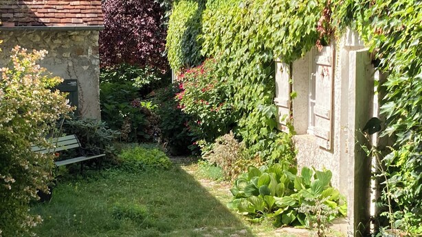 Ein Garten mit einer Steinsitzbank, üppigem Grün und einer Backsteinmauer.