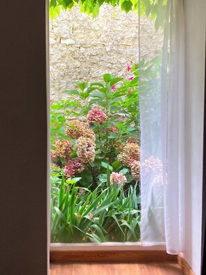 A window with a view of a garden, a stone wall, and a wooden floor. - Beaugency "la Conserverie" Entre Ville et Campagne (Beaugency)