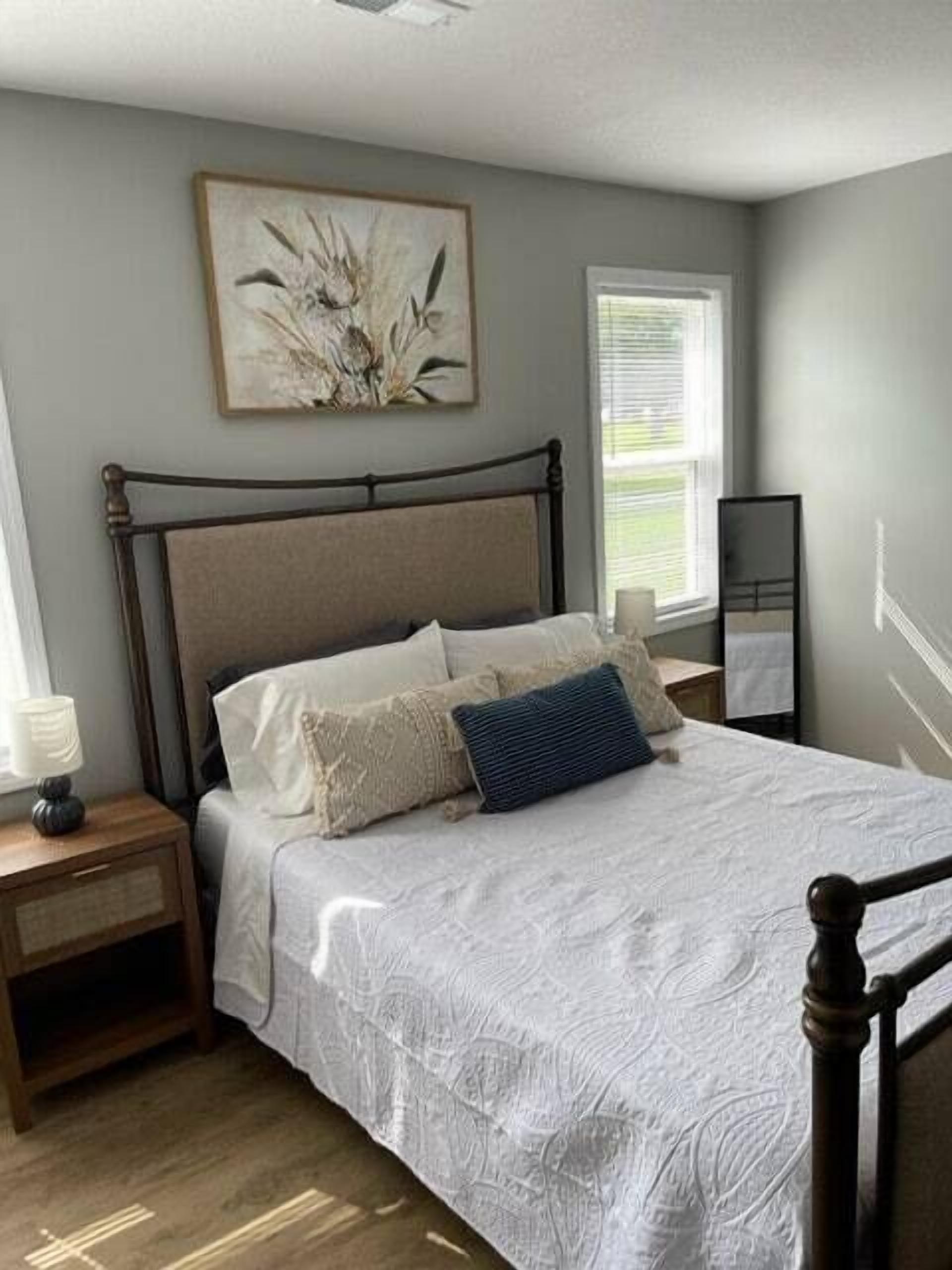 A bedroom with a bed, a nightstand, a bedside table, a mirror, and a window.