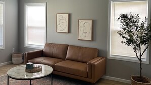 Un salon avec un canapé en cuir marron, une table basse en marbre, un tapis à motifs, un lustre et deux tableaux abstraits accrochés au mur.