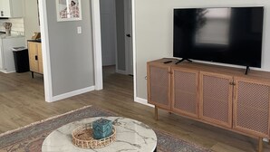 Un salon avec une table basse en marbre, un téléviseur posé sur un meuble en bois et un tapis à motifs.