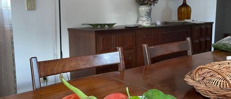 A dining table with a fruit bowl containing various fruits and a wicker basket.