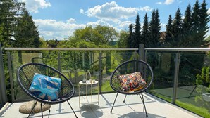 Ein Balkon mit zwei Stühlen, einem kleinen Tisch und einem Glasgeländer mit Blick auf einen Garten.