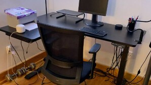 Un espacio de trabajo en casa con escritorio, silla, ordenador y diversos útiles de oficina.