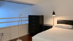 Un dormitorio con cama, cómoda, mesita de noche, lámpara y una alfombra mullida blanca.