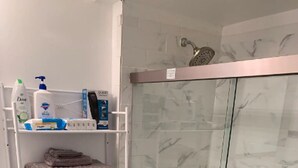Un baño con ducha de vidrio, inodoro y repisas con artículos de aseo.