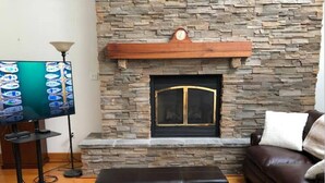 Una sala de estar con chimenea de piedra, televisor y sofá de cuero.