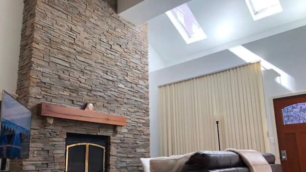 Una sala de estar con chimenea de piedra, un sofá de cuero y un ventanal con persianas.